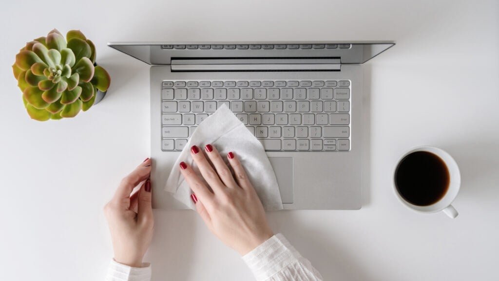 A woman worker cleaning with antivirus wet wipe a laptop and a working office desk before starting work for protect herself from bacteria and virus.