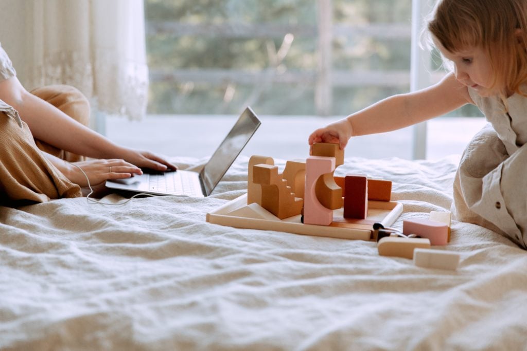 Child playing on bed while parent works on computer